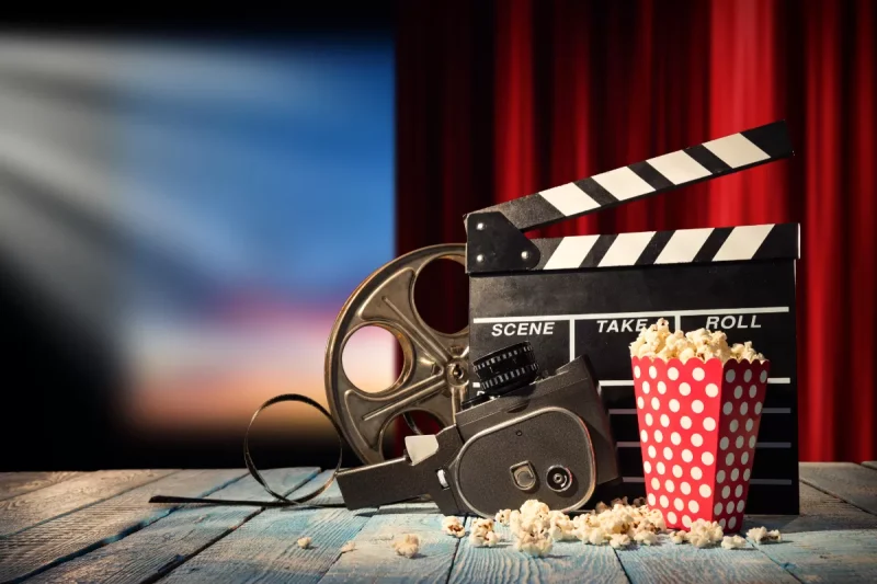 Retro film production accessories placed on wooden planks. Concept of film-making. Red curtain and movie screen on background