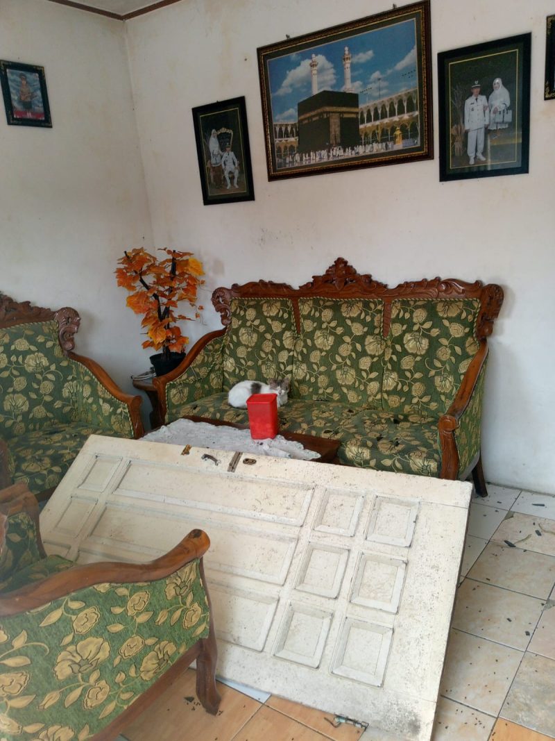 Kondisi Pasca Pengrusakan Rumah Korban, nampak Pintu jebol tergletak di antara meja ruang tamu, Kaca jendela berserakan di halaman rumah